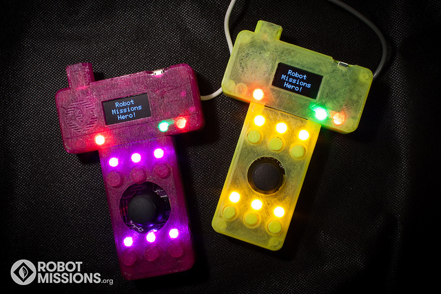 Two of the Operator Interfaces, with the LEDs glowing, and display showing 'Robot Missions Hero!'
